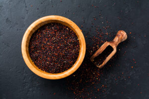 Black quinoa grains seeds in a bamboo bowl on a black stone background. Flat lay with copy space.